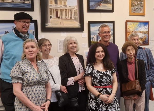A group of art class students smile at the camera while stood in front of artwork in a gallery